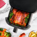 Detailní pohled na TESLA AirCook Q60 XXL Pro fritézu při pečení celého kuřete se zeleninou, v průhledné zásuvce zařízení.